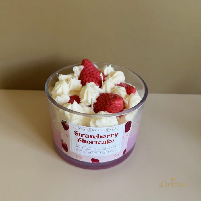 Candle in a glass jar with strawberries and whipped cream on top, labeled 'Strawberry Shortcake', against a plain background.