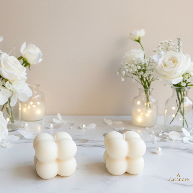 Two white bubble-shaped candles on a white surface with flowers and lights in the background, featuring the brand 'Lavanore'. Lumi Bubble sculptural bubble soy wax candle for luxury gifting and modern home décor