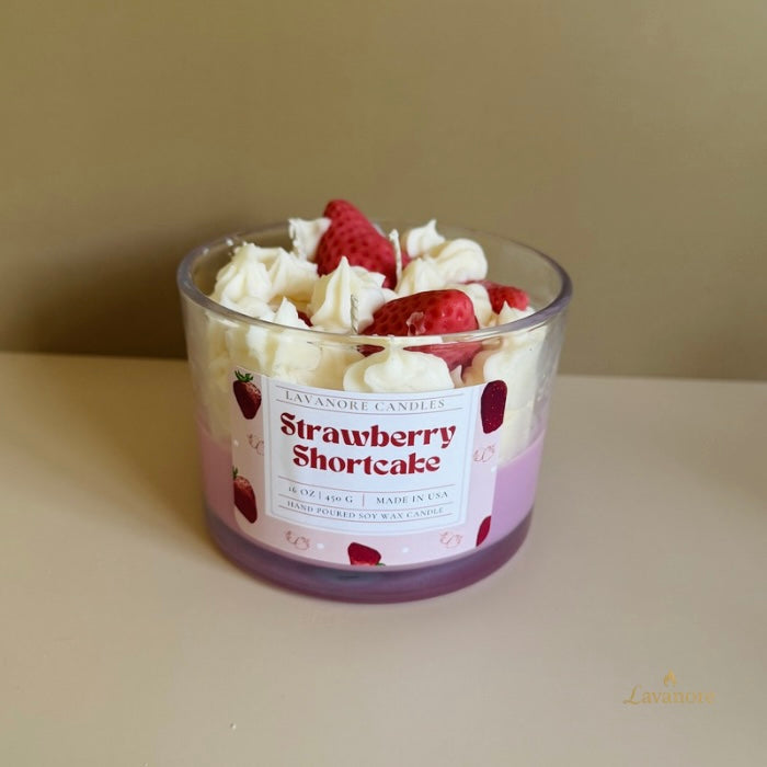 Candle in a glass jar labeled 'Strawberry Shortcake' with whipped cream and strawberries on top.