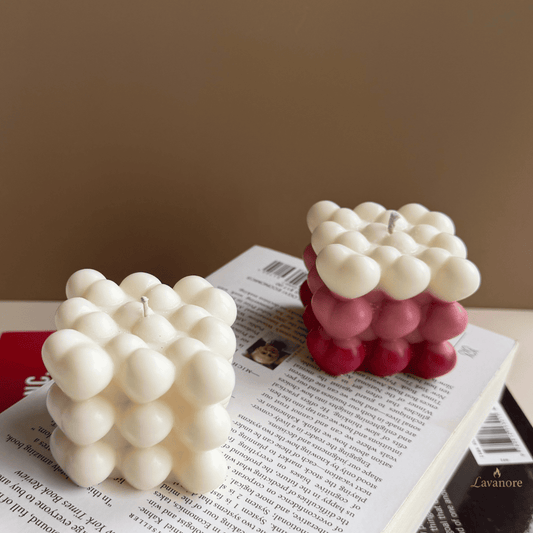 Two bubble-style candles, one white and one pink, on top of a book with a plain background. Sculptural heart bubble candle handcrafted in clean soy wax
