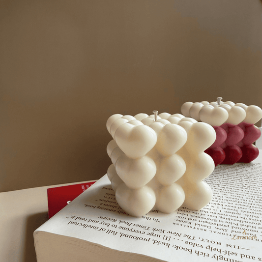 White bubble candle on an open book with a beige background. Sculptural heart bubble candle handcrafted in clean soy wax