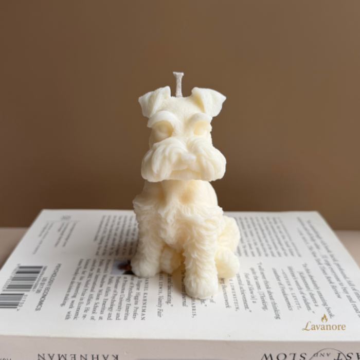 Dog-shaped candle on a book with a plain background. Schnauzer sculptural soy wax candle designed for luxury gifting and modern home décor