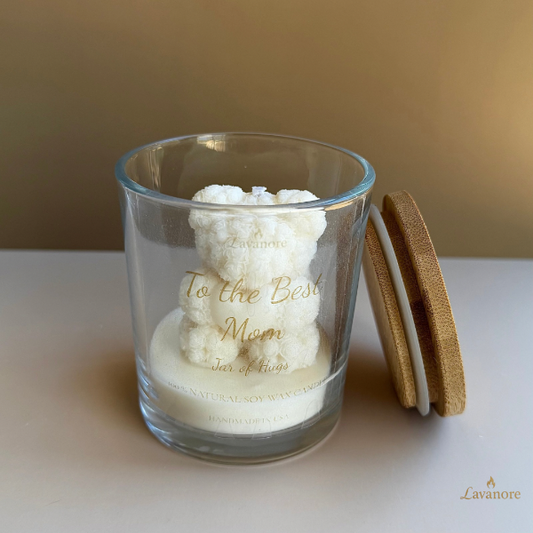 Glass candle with a wooden lid on a white surface, featuring 'To the Best Mom' text. Jar of Hugs teddy bear sculptural soy wax candle in glass jar for luxury gifting